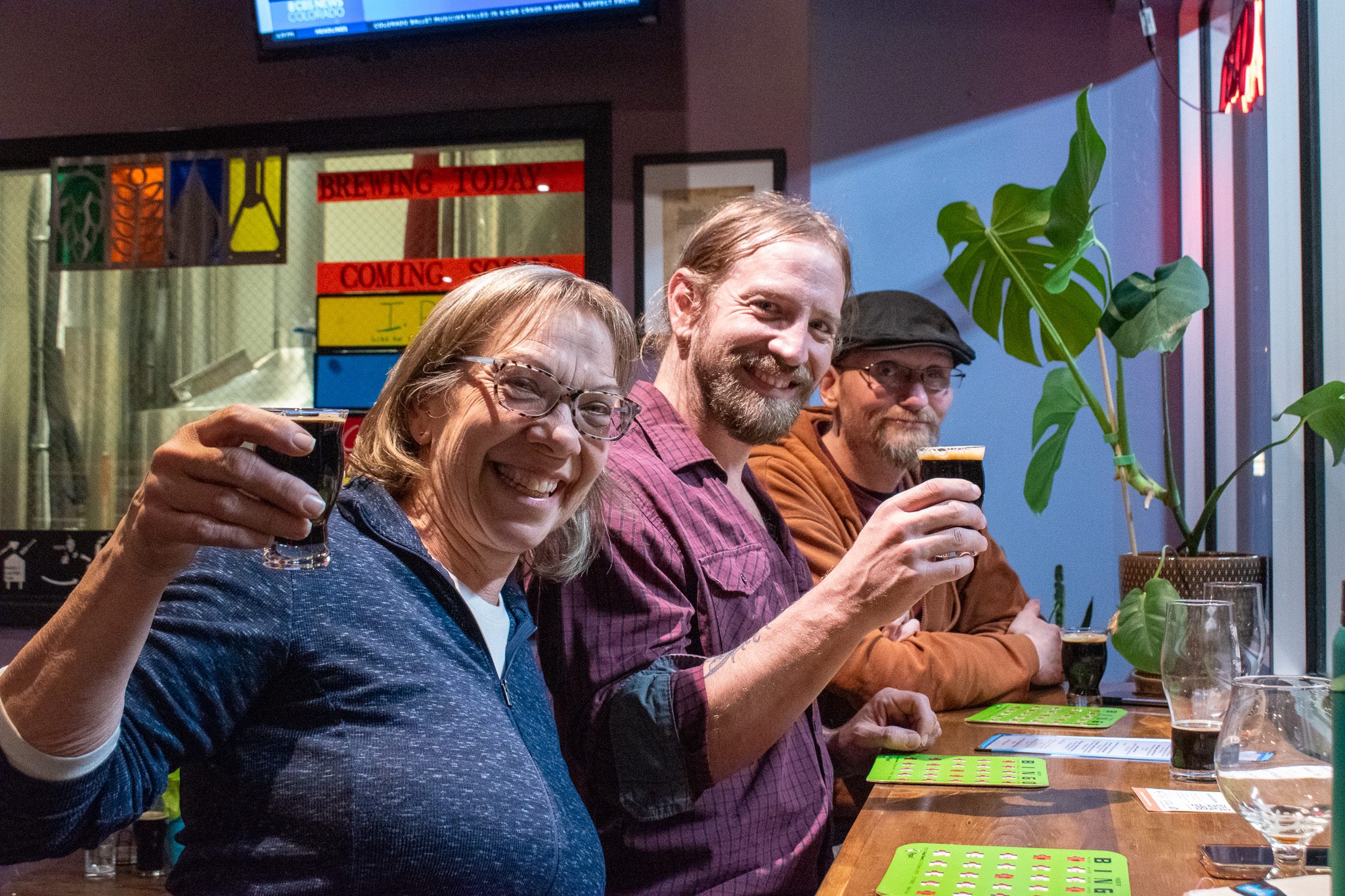 three friends smiling for a photo and holding up their beers at a brewery