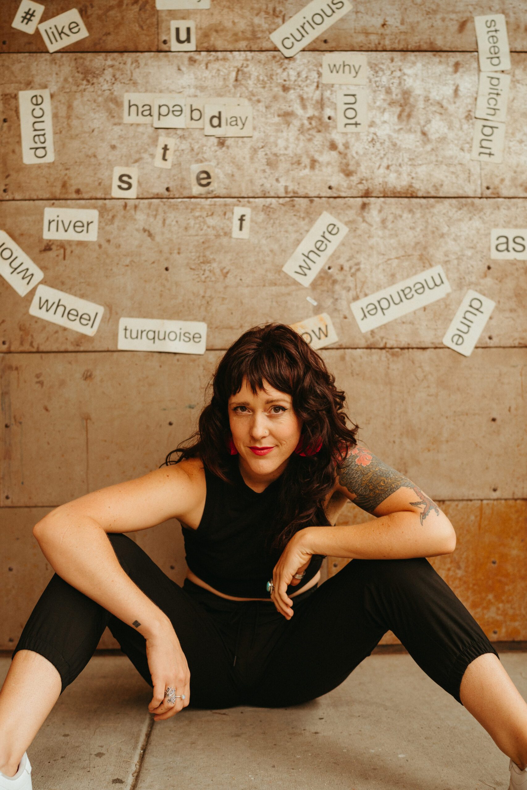 poet ally eden smiling for a photo in front on a wall with various words on it