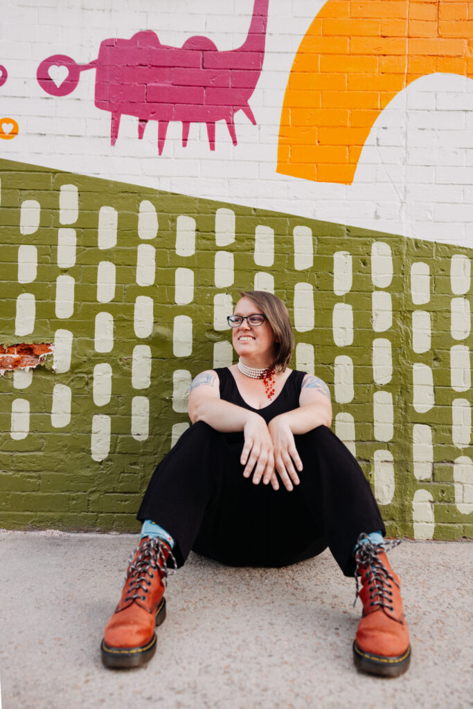 author lindsay king miller seated on the ground in front of a colorful mural