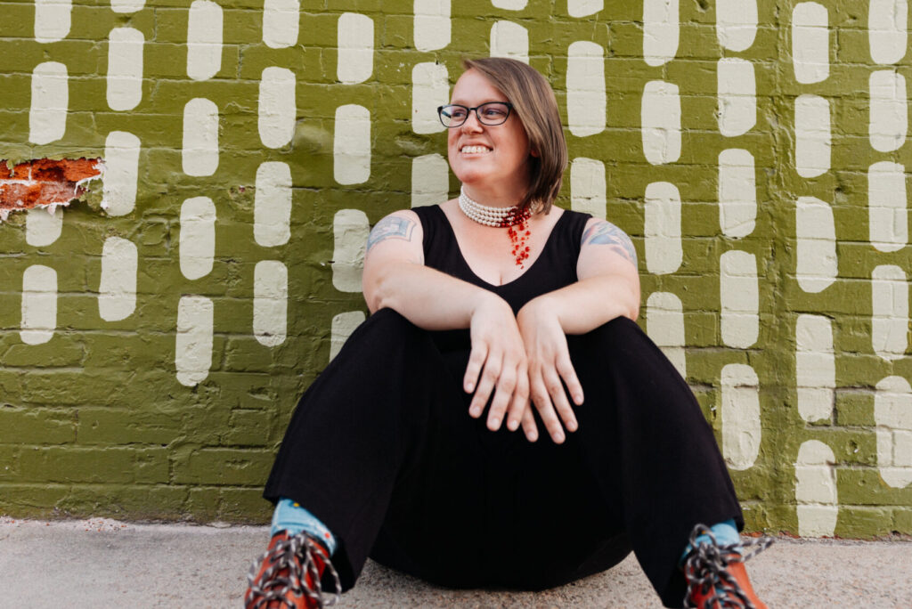 author lindsay king miller seated on the ground in front of a colorful mural