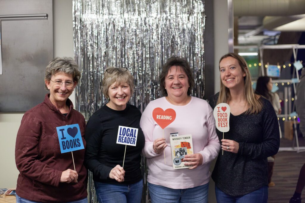 four women smiling for a photo holding book themed signs